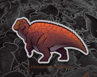 May include: A sticker featuring a cartoon illustration of a Kritosaurus navajovius dinosaur. The dinosaur is depicted in shades of orange and brown with a textured pattern on its back. The sticker has a white border and is set against a background of other dinosaur stickers.