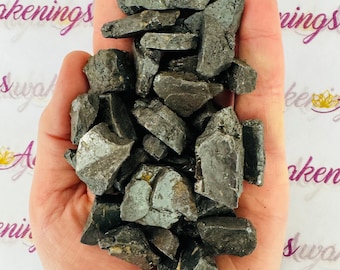 May include: A hand holding a pile of small, dark gray, rough, and jagged pieces of black obsidian.