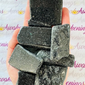 May include: A collection of seven dark green and black polished stones, likely a type of slate or schist, arranged in a pile in a person's hand.