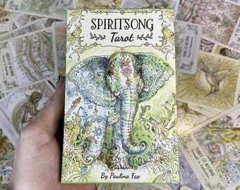 Może przedstawiać: Talia kart Tarota SpiritSong z akwarelową ilustracją słonia z misternymi wzorami i kwiatowym wzorem. Tekst "SpiritSong Tarot" i "By Paulina Fae" jest nadrukowany na karcie.