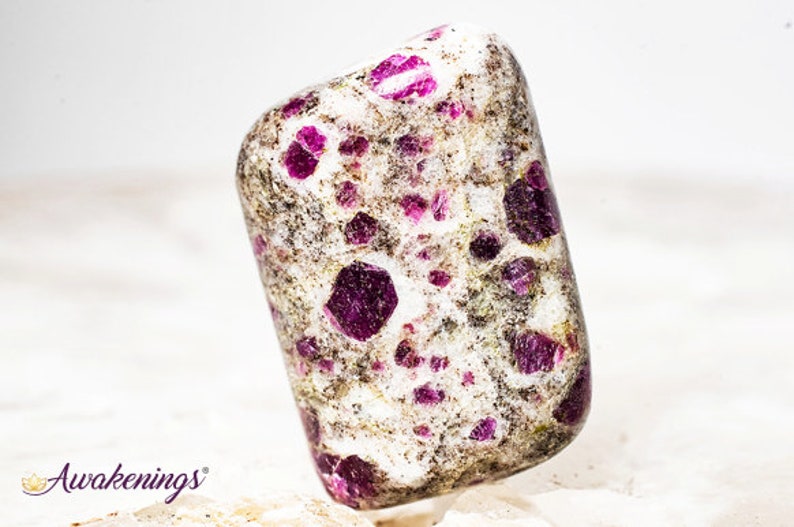 May include: A white tumbled stone with a high concentration of small, deep pink ruby inclusions. The stone has a speckled appearance.
