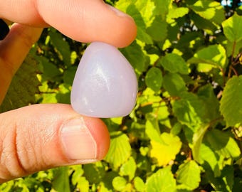 May include: A smooth, light purple tumbled stone with a slight sheen. The stone is about the size of a quarter and is held in a hand.