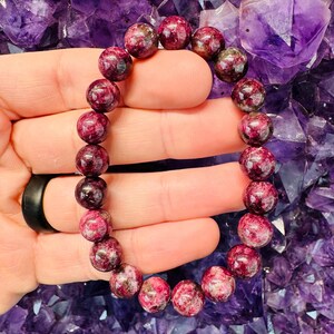 May include: A pink and green gemstone bracelet with round beads. The bracelet is made of natural stones and is approximately 7 inches in length.