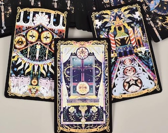 May include: A tarot card deck with detailed illustrations. The cards have a black background with gold borders and vibrant imagery, including stars, geometric shapes, and symbolic figures. The cards are arranged on a light surface.