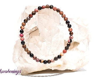 May include: A pink, brown, and black beaded bracelet with a stretchy elastic cord. The bracelet is made with natural stones and is displayed on a white rock.