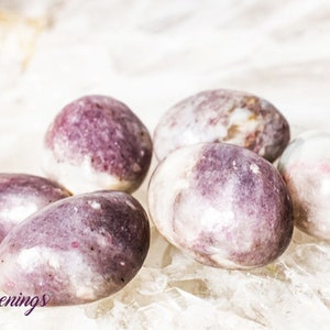 May include: Five smooth, polished, purple and white Lepidolite tumbled stones. The stones are oval shaped and have a natural, organic look.