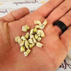 Könnte beinhalten: Ein kleiner Haufen hellgrüner und weißer Kristallsplitter in einer Hand. Die Kristalle sind unregelmäßig geformt und haben eine raue Textur.