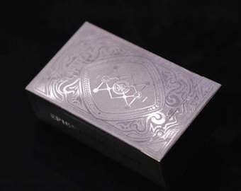 Könnte beinhalten: Eine silberne Spielkartenbox mit einem komplizierten geometrischen Design und dem Wort "SPIRIT" auf der Vorderseite.