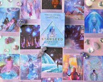 May include: A colorful oracle card deck with a guidebook titled "The Starseed Oracle: A 53 Card Deck & Guidebook". The cards feature celestial imagery and text such as "Breath of the Cosmos", "Star Family", and "Deep Cellular Healing".