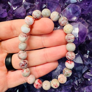 May include: A bracelet made of red, white, and gray gemstone beads. The beads are round and have a speckled pattern.