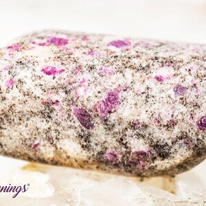 May include: A close-up of a tumbled stone with a white base and pink and black flecks.