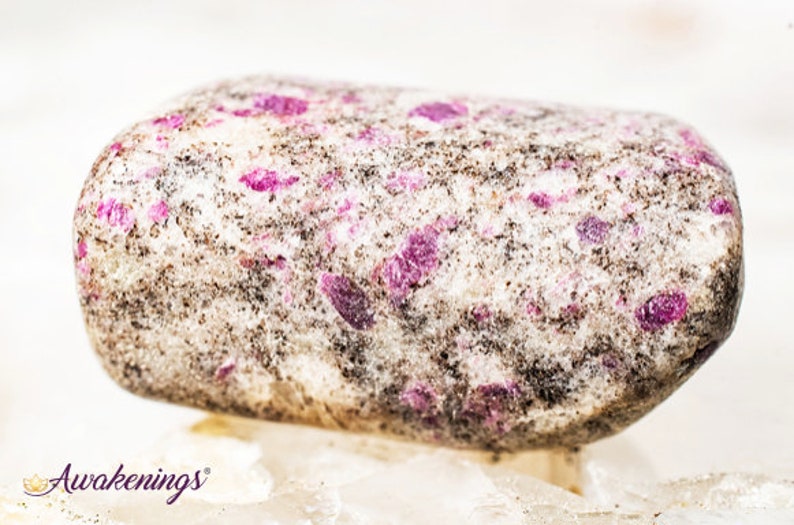 May include: A close-up of a tumbled stone with a white base and pink and black flecks.