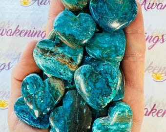 Peut inclure: Plusieurs pierres en forme de cœur, dans des tons de turquoise, de vert et de bleu sarcelle. Les pierres ont un aspect marbré avec des variations naturelles de couleur et de texture. Le fond porte le mot "Awakenings" en écriture cursive.