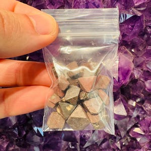 May include: A small plastic bag filled with a collection of small, dark brown, pyramid-shaped crystals.