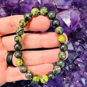 Pode incluir: Um bracelete de pedras preciosas verde e preto com contas redondas. O bracelete é feito de pedras naturais e tem aproximadamente 18 cm de comprimento.