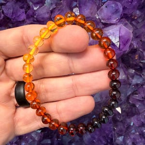 Peut inclure: Un bracelet de perles circulaire présentant un dégradé de couleurs de perles translucides. Les perles passent d'un jaune-orange vif à une extrémité à un brun profond et noir à l'autre, créant un effet ombré lisse sur toute la pièce.