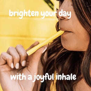 Puede incluir: Una persona con cabello largo y castaño sostiene una pajita amarilla en su boca. El fondo es amarillo y el texto "brighten your day with a joyful inhale" está escrito en blanco.