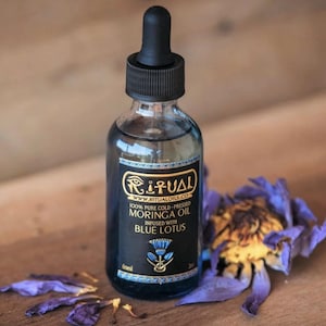 May include: A clear glass bottle of Ritual Moringa Oil with a black dropper top. The label reads "100% Pure Cold-Pressed Moringa Oil Infused with Blue Lotus." A blue lotus flower and petals are next to the bottle.