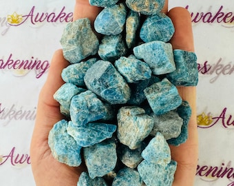May include: A handful of rough, blue-green apatite stones. The stones have a natural, unpolished appearance with varying shades of blue and gray. The background has the word "Awakenings" in a script font.