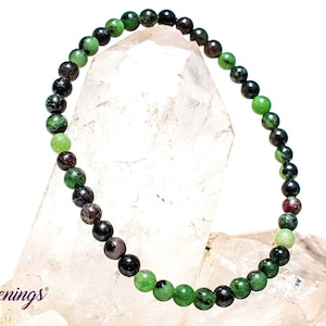 May include: A green, black, and pink gemstone bracelet with round beads. The bracelet is on a white background.