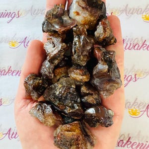 Puede incluir: Un puñado de piedras de ágata marrones, blancas y grises. Las piedras son ásperas y tienen un aspecto natural sin pulir.