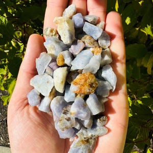 May include: A handful of blue, purple, and brown rough sapphire gemstones. The stones are various sizes and shapes.