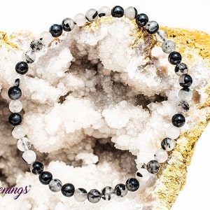 May include: A black and clear crystal beaded bracelet with alternating black and clear beads. The bracelet is lying on a white and gold rock.