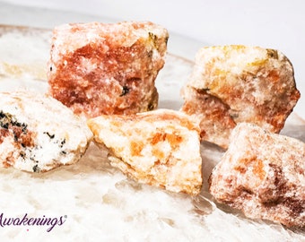 May include: Five rough, natural, pink and orange selenite crystals on a white surface. The crystals are various sizes and shapes.