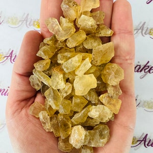 May include: A hand holding a pile of small, translucent, yellow-brown crystals. The crystals are irregularly shaped and have a slightly rough texture.