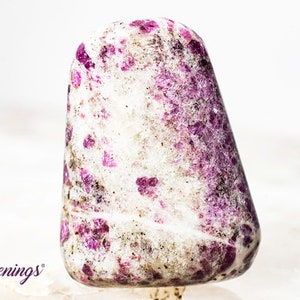 May include: A white and pink tumbled stone with a speckled pattern. The stone is smooth and polished.