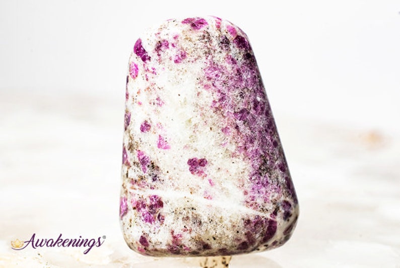 May include: A white and pink tumbled stone with a speckled pattern. The stone is smooth and polished.