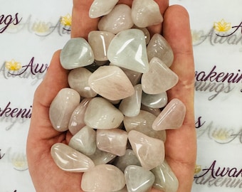 May include: A hand holding a collection of tumbled, light green and pink stones. The stones are smooth and have a natural, polished finish.