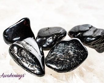 May include: Five smooth, black hematite stones, also known as bloodstone, on a white background. The stones are various shapes and sizes.