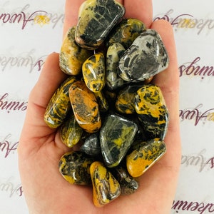 May include: A collection of tumbled yellow and black bumblebee jasper stones. The stones are smooth and polished, with a variety of patterns and colors.