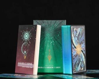 May include: A tarot card set with a burgundy instruction booklet, a green box with a sunburst design, and a deck of cards with blue edges. The box is labeled "BROKEN MIRROR TAROT". The cards feature celestial and geometric designs.