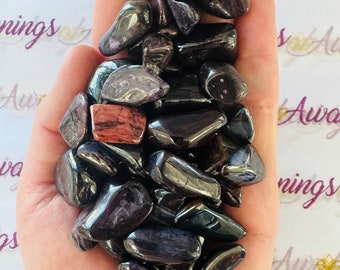 May include: A collection of tumbled black and purple stones with a few red and pink stones mixed in. The stones are smooth and polished.
