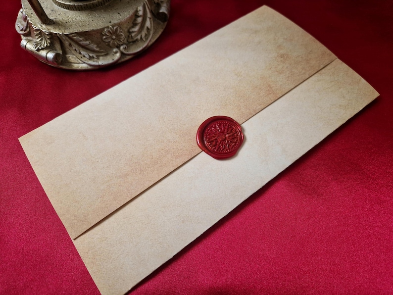May include: A vintage-style envelope with a red wax seal. The envelope is made of aged, tan-colored paper with a darker, faded border. The seal is circular, with a detailed design. The envelope is on a red surface.