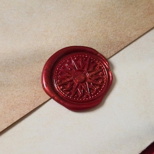 May include: A detailed, red wax seal with a compass rose design. The seal is affixed to a light-colored paper, suggesting a vintage or nautical theme. The wax has a glossy finish, and the design is intricate.