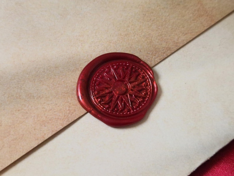 May include: A detailed, red wax seal with a compass rose design. The seal is affixed to a light-colored paper, suggesting a vintage or nautical theme. The wax has a glossy finish, and the design is intricate.