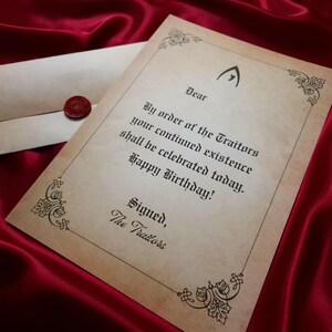 May include: A parchment-style birthday card with an envelope, sealed with a red wax stamp, rests on a deep red satin surface. The card features ornate borders and gothic-style text that reads "By order of the Traitors...Happy Birthday!"