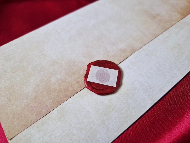 May include: An envelope with a red wax seal. The envelope is off-white and tan, with a diagonal seam. The seal is red with a small white square in the center.