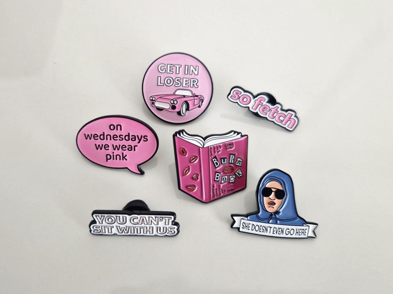Puede incluir: Conjunto de seis pines de esmalte con citas e im&aacute;genes populares de la pel&iacute;cula Mean Girls. Los pines son de color rosa, blanco y azul con contornos negros. Los pines presentan el texto "Get in Loser", "On Wednesdays We Wear Pink", "You Can't Sit With Us", "So Fetch", "Burn Book" y "She Doesn't Even Go Here".