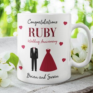 May include: White ceramic mug with a handle, featuring the words "Congratulations RUBY Wedding Anniversary" in burgundy script. The mug includes illustrations of a tuxedo and a red dress, with red heart accents. The names "Brian and Susan" are also printed on the mug.