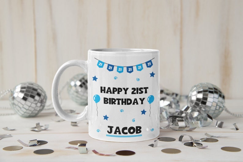 May include: White ceramic mug with a blue and white design. The mug says "Happy 21st Birthday Jacob" with blue stars and balloons.