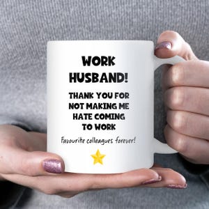 May include: White ceramic mug with the text "WORK HUSBAND! THANK YOU FOR NOT MAKING ME HATE COMING TO WORK" and "Favourite colleagues forever!" in black. A yellow star graphic is also present.