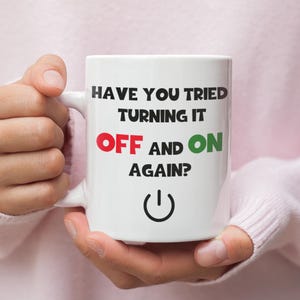 May include: White ceramic mug with the text "Have you tried turning it off and on again?" in black, red, and green. A power button symbol is below the text.