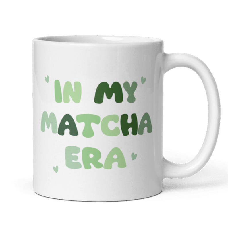 Może przedstawiać: Biały kubek ceramiczny z napisem 'In My Matcha Era' w zielono-białych literach.