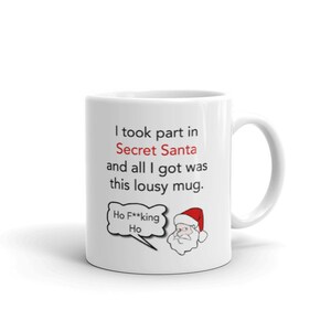 Op de afbeelding: Witte keramische mok met een humoristische boodschap over een Secret Santa cadeau-uitwisseling. De mok heeft de tekst: "Ik deed mee aan Secret Santa en alles wat ik kreeg was deze waardeloze mok." Er is ook een cartoon van de kerstman afgebeeld.
