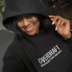 Könnte beinhalten: Schwarzer Kapuzenpullover mit dem Text "OVERDRAFT INSUFFICIENT FUNDS AVAILABLE" in weiß auf der Vorderseite gestickt.