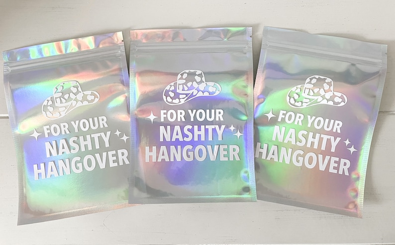 以下が含まれることがあります： 「FOR YOUR NASHTY HANGOVER」の白い文字が入った、3つの虹色のポーチ。各ポーチには白いカウボーイハットのグラフィックがあります。ポーチはジッパーで密封されています。
